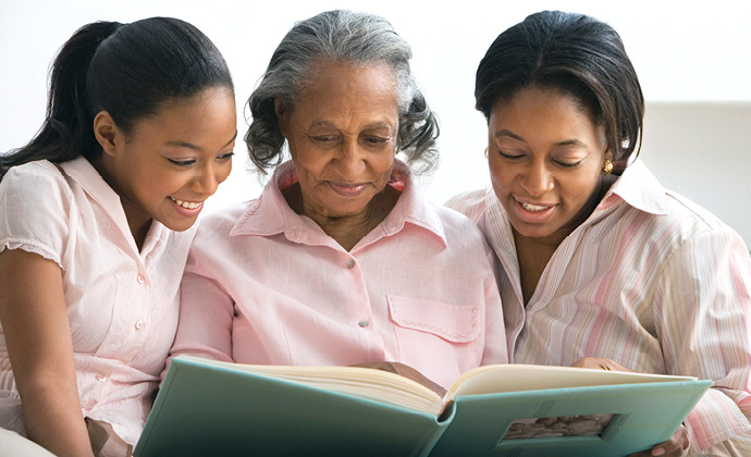 A woman looks at a family photo album with her two granddaughters