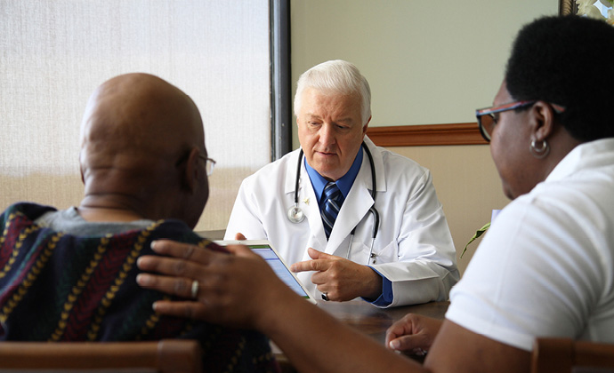 A VITAS physician shares information on a tablet with a couple sitting in his office