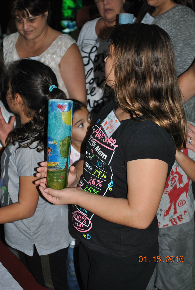 A girl holds a candle with a decorative cover honoring a loved one
