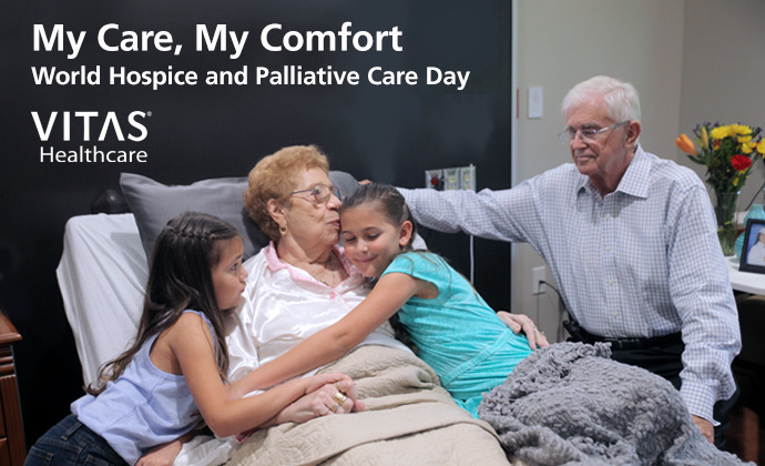 A woman in bed embraces her two granddaughters as her husband looks on, with the words "My Care, My Comfort: World Hospice and Palliative Care Day" on the image