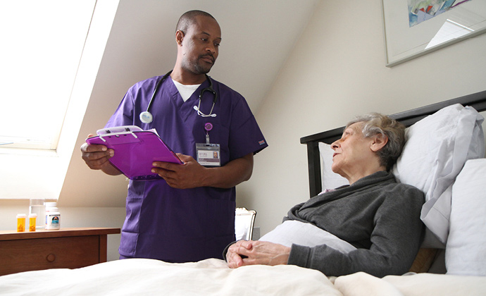 A VITAS nurse talks with a patient as she sits up in bed