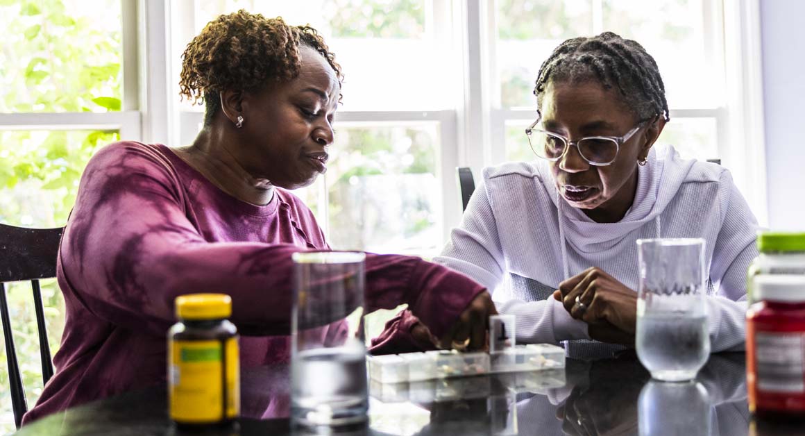 A lesbian couple sort pills into a weekly organizer at their kitchen table