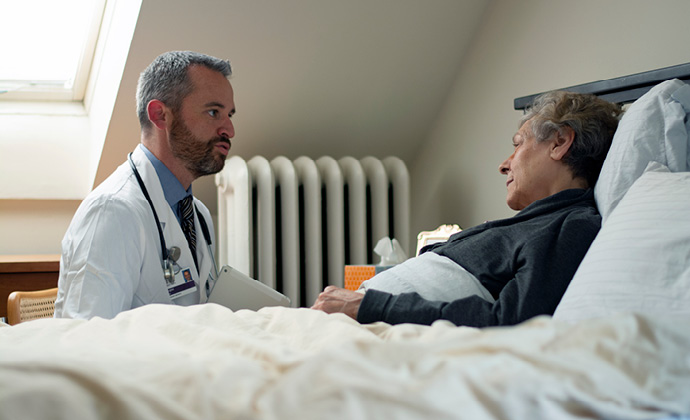 A VITAS physician speaks with a woman who is lying in bed