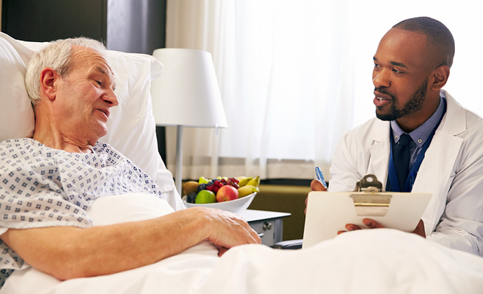 A man sitting up in bed talks with his physician